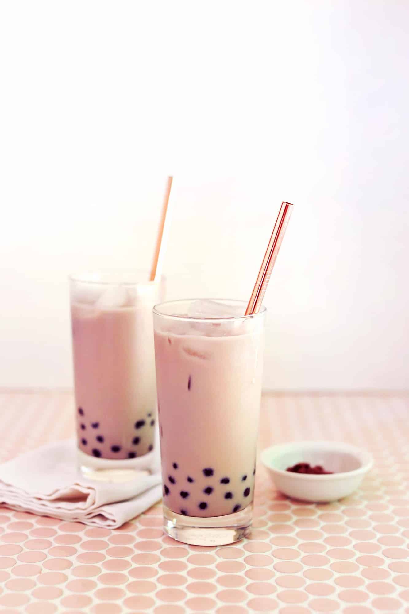 2 glasses of iced chai tea with boba pearls and gold straws in it
