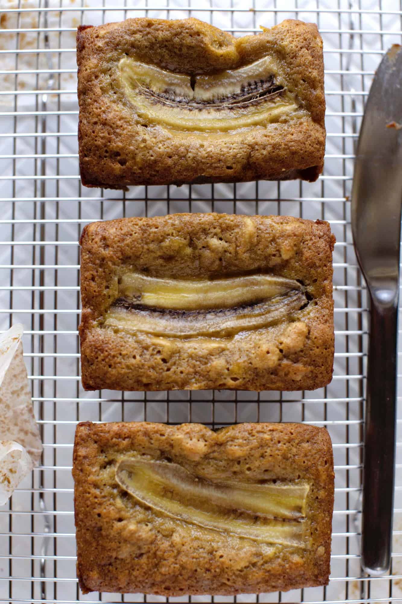 3 loaves of banana bread and a knife on a cooling rack